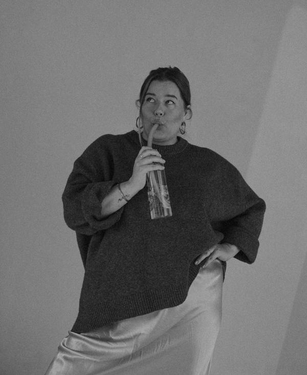 a woman in a sweater and satin skirt is drinking from a glass through a straw .