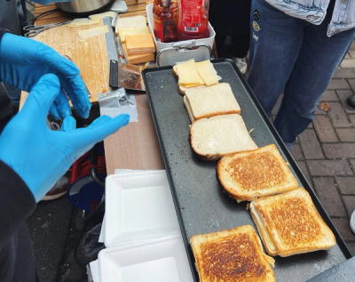 a person making grilled cheese sandwiches wearing blue gloves reaches for a bottle of ketchup