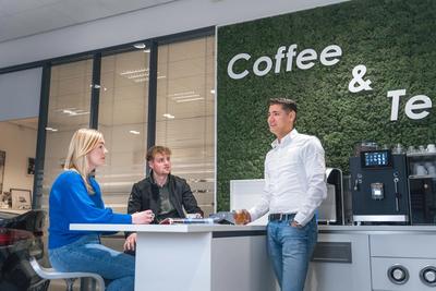 a group of people are sitting at a table in front of a coffee and tea wall .