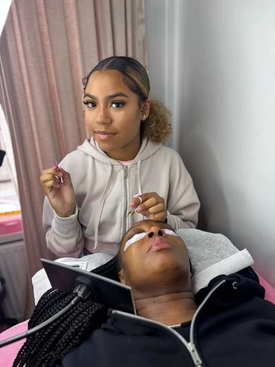 a woman is sitting next to a woman who is getting eyelash extensions .