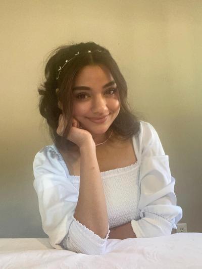 a woman wearing a white top and a headband is sitting at a table with her hand on her chin .