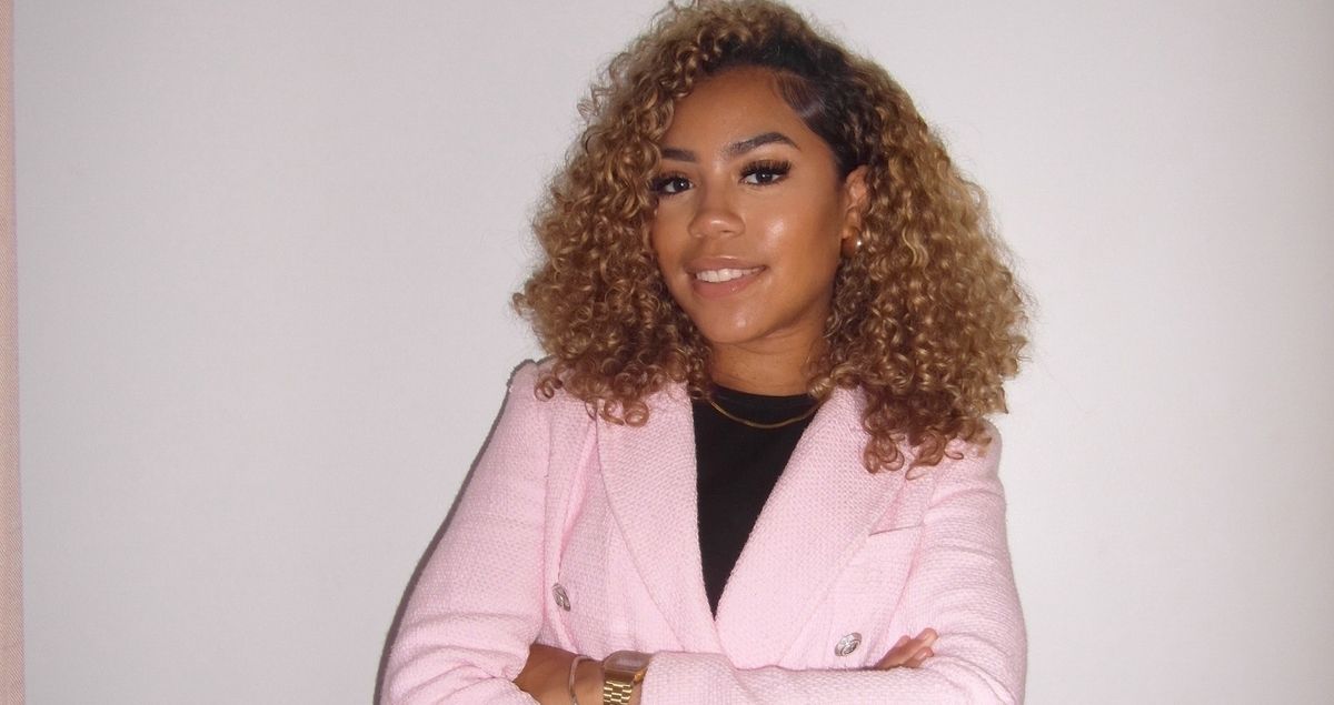 een vrouw met krullend haar draagt een roze blazer