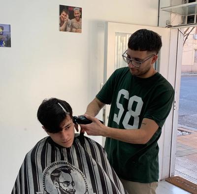 un hombre se está cortando el pelo con un barbero que lleva una camisa verde con el número 58 .