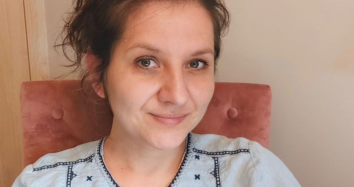 Zsuzsanna wearing a blue shirt is sitting in a pink chair