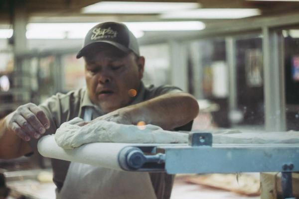 Man kneading dough on conveyor belt