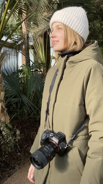 a woman in a green coat is holding a sony camera
