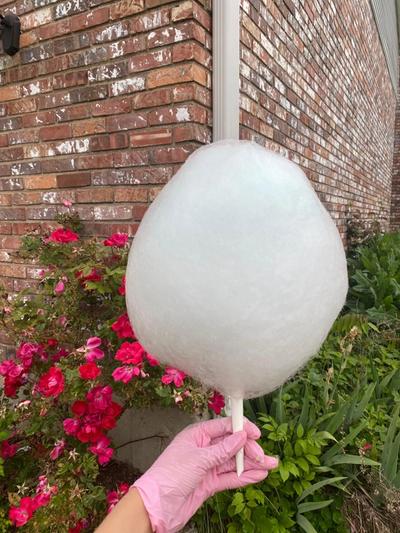 a person wearing pink gloves is holding a large cotton candy on a stick .