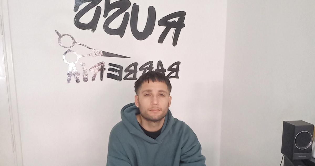 un hombre sentado en un mostrador frente a una pared que tiene escrita la palabra barbero