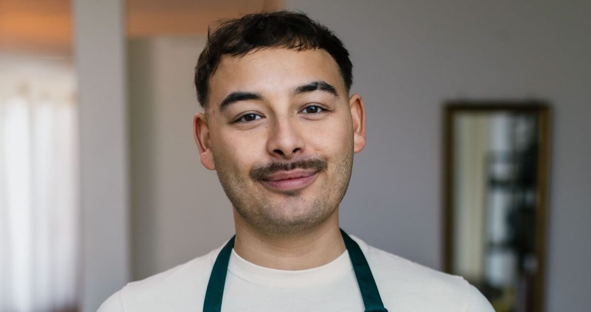 a man in an apron is holding a sandwich on a cutting board