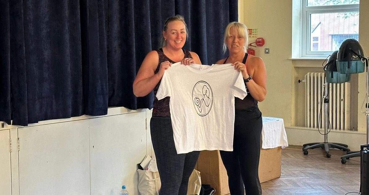 two women are holding a white t-shirt in a room .