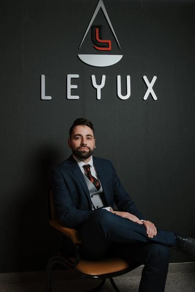 a man in a suit and tie is sitting in front of a sign that says leyux