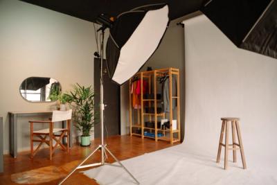 a photo studio with a stool , chair , mirror and clothes rack .