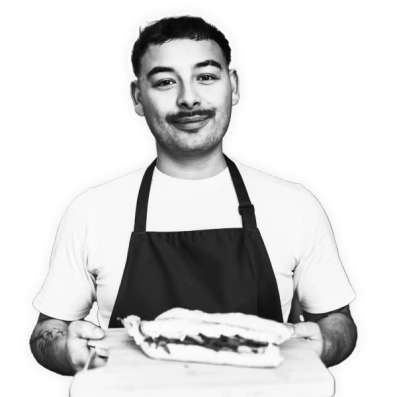 a man in an apron is holding a sandwich on a cutting board .