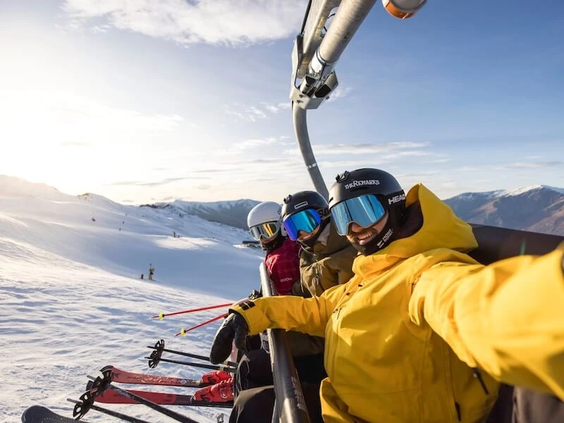 A selfie of a group of adventure travellers on a ski life at golden hour on a mountain in Queenstown, while on a ski tour with Wild Kiwi.