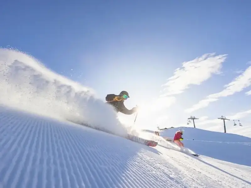 Skiers carving fresh powder on a bluebird day at a New Zealand ski resort in the South Island during winter.