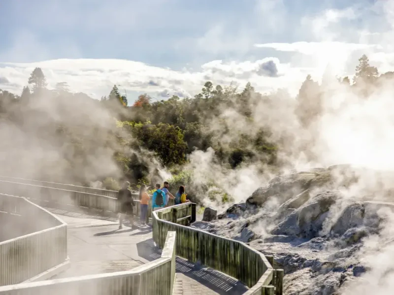 Travellers walking through a steaming geothermal area in Rotorua, showing one of the best North Island winter activities in New Zealand with hot springs, volcanic landscapes, Māori cultural experiences and all-weather winter travel appeal.