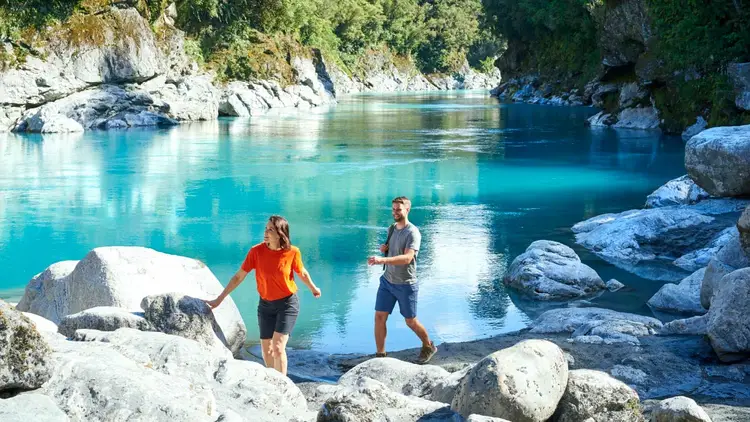 Two people walking next to an icy blue river