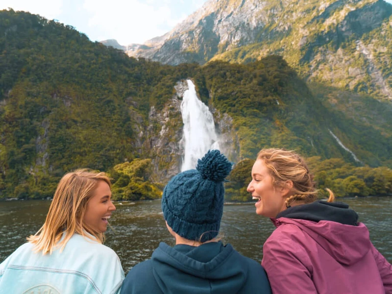 A group of female travellers on a Milford Sound cruise in Autumn laugh and enjoy the weather while visiting on their Wild Kiwi small group tour of the South Island.