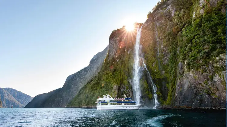 A cruise boat under a waterfall in Milford Sound