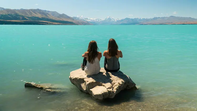 Two people sitting on a rock in Lake Tekapo