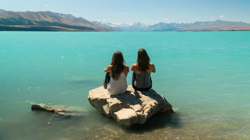Two friends sitting on a rock in Lake Tekapo
