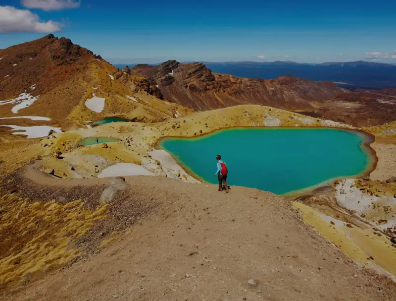 Person walking next to an alpine lake on the Tongariro Crossing