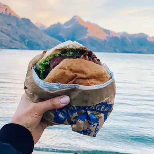 Person holding a fergburger in front of Lake Wakatipu