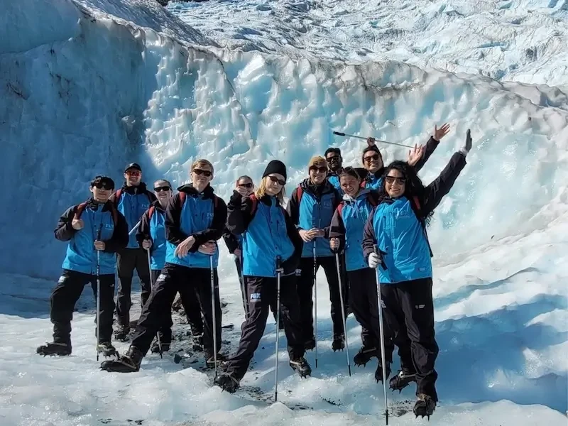 Group of travellers on a guided glacier hike in Franz Josef, New Zealand, wearing crampons and winter gear in an icy alpine landscape.