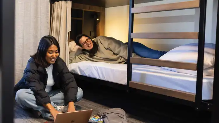 Two women sitting on a dorm bed in a hostel 