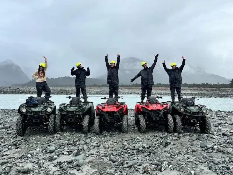 Group of travellers standing on quad bikes during an off-road ATV adventure tour in New Zealand’s South Island with scenic mountain backdrop.