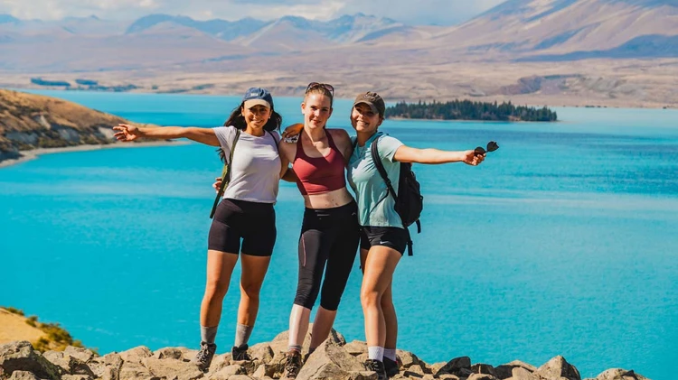 Three women pose for a photo in front of Lake Tekapo