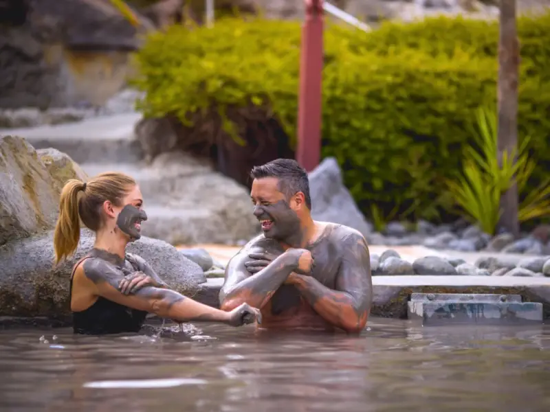 Travellers relaxing in a steaming geothermal hot pool in New Zealand, highlighting hot pools as one of the best winter activities beyond skiing, with mineral mud, warm water and a peaceful wellness experience ideal for a New Zealand winter travel itinerary.