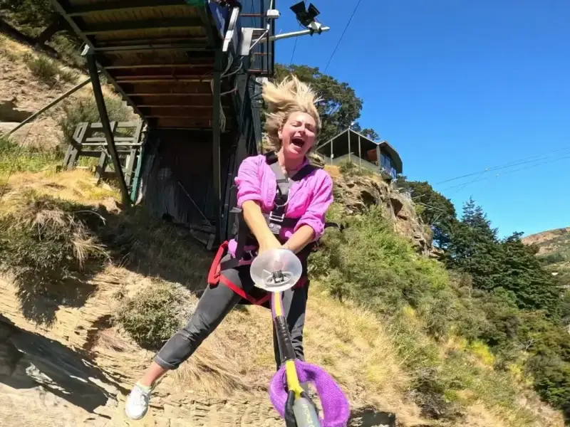 Traveller bungee jumping in Queenstown, New Zealand, screaming mid-jump in a harness against blue sky and alpine hills — iconic South Island adventure activity for thrill-seekers.