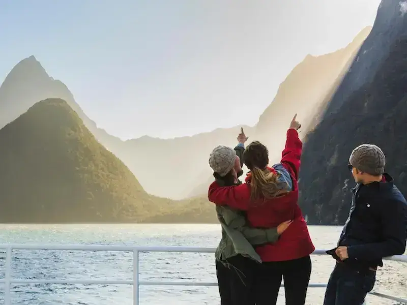 Three travellers look up at the stunning waterfalls of Milford Sound from a cruise while on a small group day tour from Queenstown.