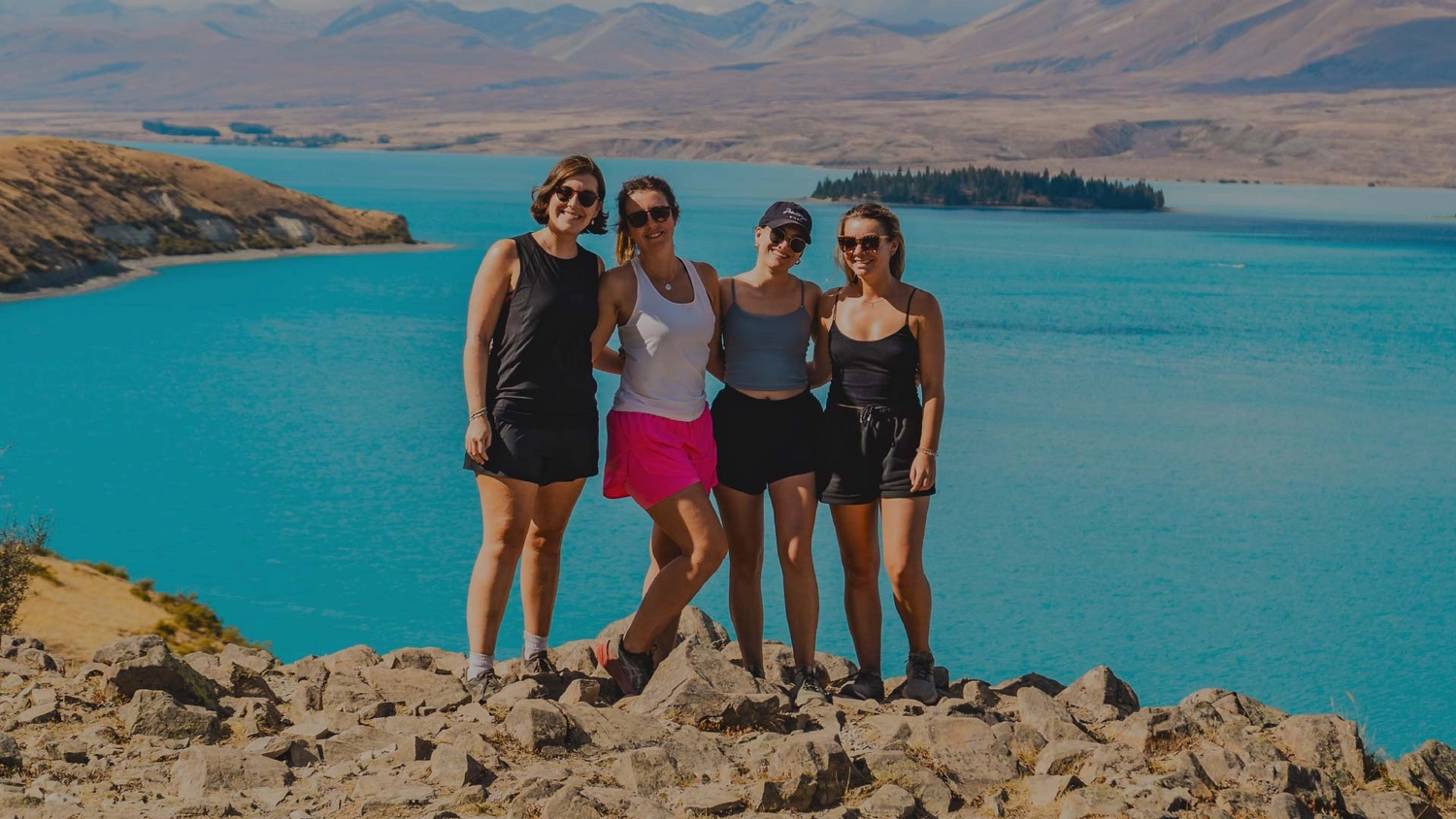 Four women posing for a photo in front of Lake Tekapo