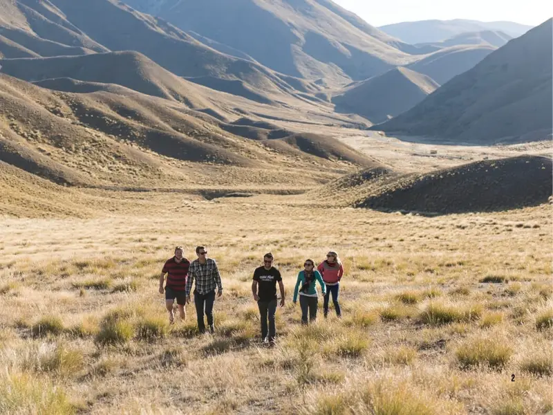 A small group of travellers walking through New Zealand’s South Island high country, with golden tussock grass, mountain valleys and remote hiking scenery featured in Wild Kiwi adventure tours.