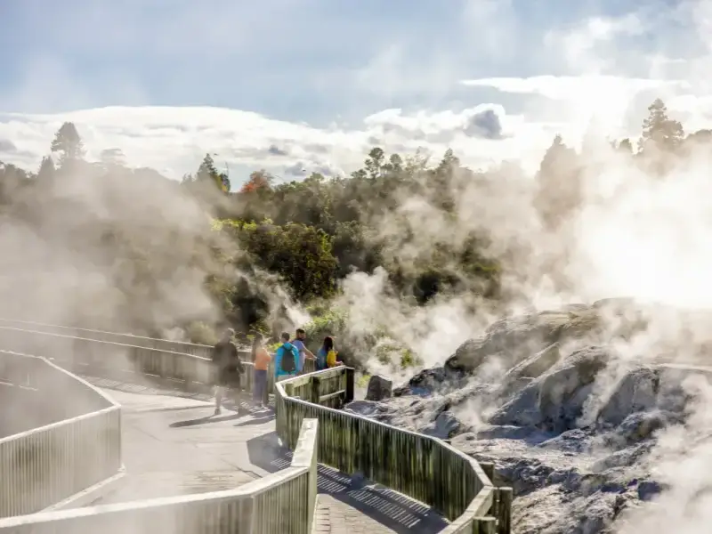Travellers walking through a steaming geothermal area in Rotorua, showing one of the best North Island winter activities in New Zealand with hot springs, volcanic landscapes, Māori cultural experiences and all-weather winter travel appeal.