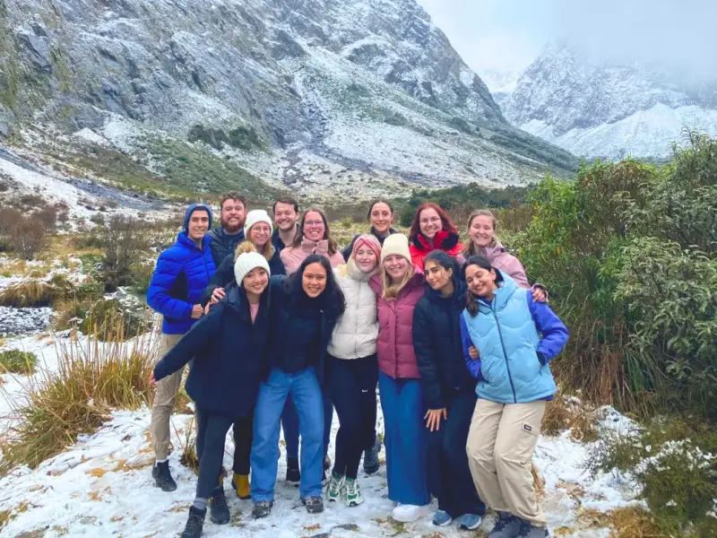 Small group of travellers standing together in a snowy mountain valley in New Zealand, showing a social winter travel experience with alpine scenery, cold-weather layers and South Island adventure beyond the ski fields.