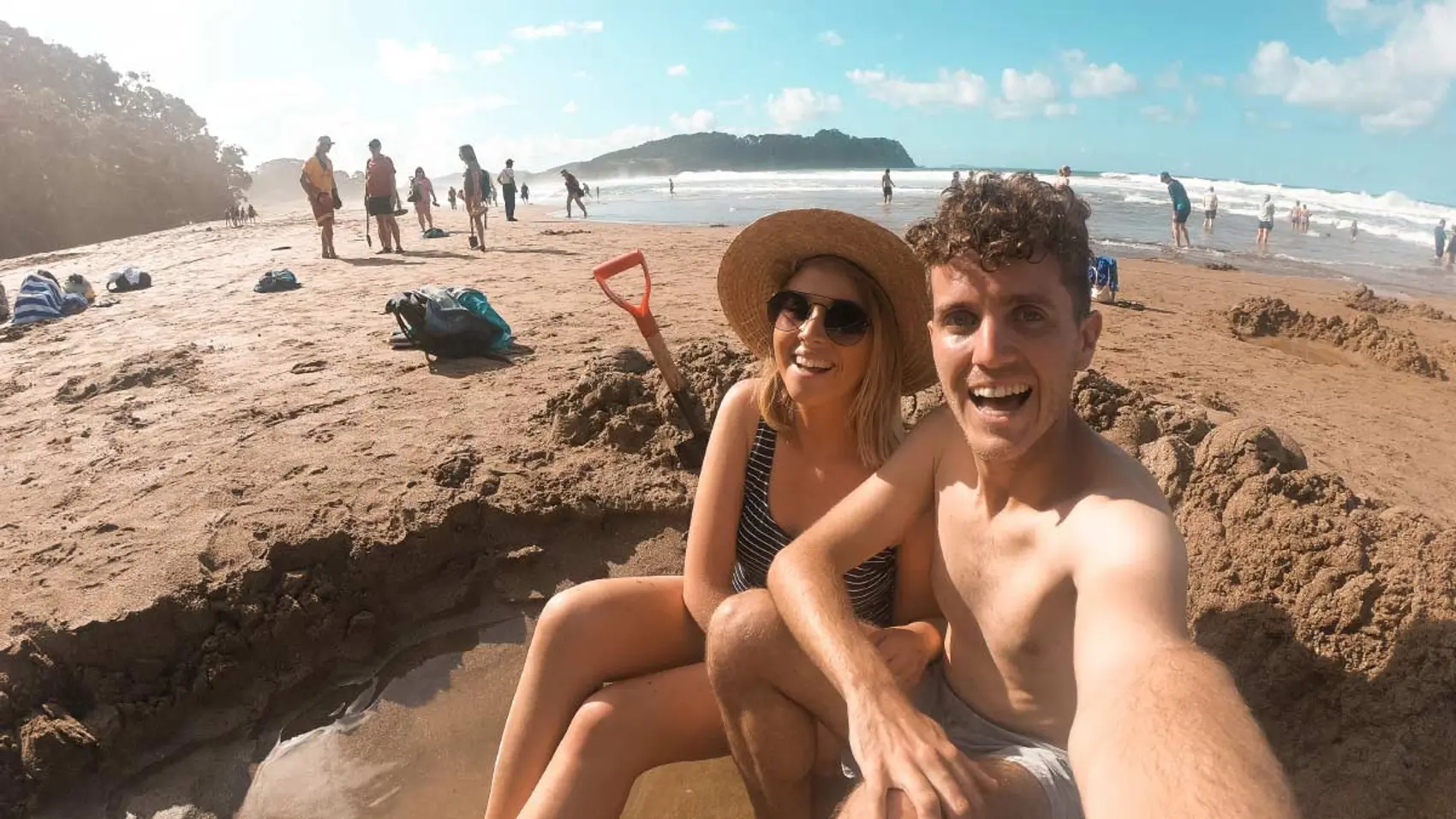 Couple sit in a hole in the sand on Hot Water Beach