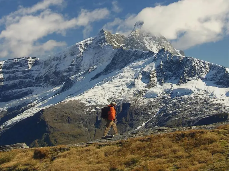 A solo hiker crossing an alpine track beneath snow-covered peaks in New Zealand’s South Island, representing the mountain scenery, adventure travel and challenging hiking trails found across New Zealand.