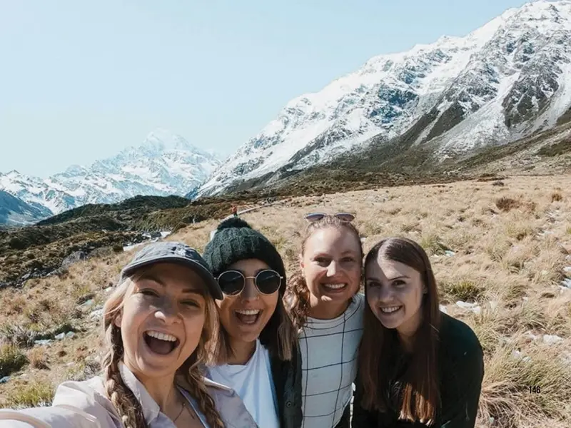 Wild Kiwi travellers smiling in front of dramatic South Island mountain scenery, showing the kind of alpine landscapes, outdoor adventure and group travel experiences that help make the South Island one of the best choices for a New Zealand road trip or small group tour.