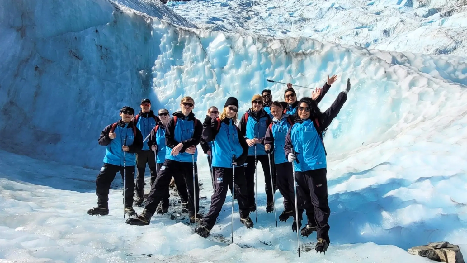 A group of happy travellers on a flashpacking small group tour of New Zealand stand atop a glacier in Franz Josef.
