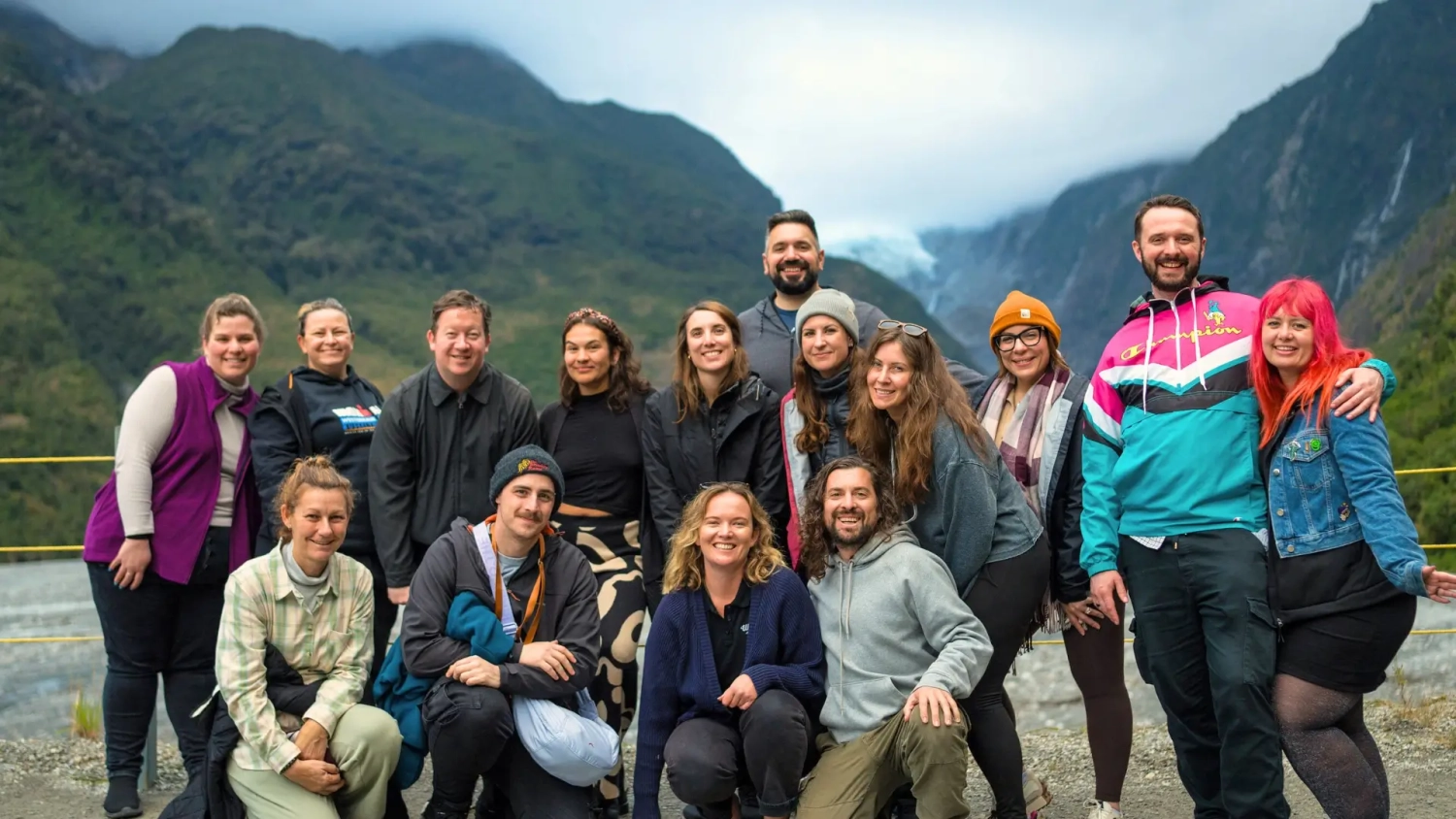 Group of smiling travellers on a Milford Sound day trip from Queenstown posing in front of Fiordland National Park.