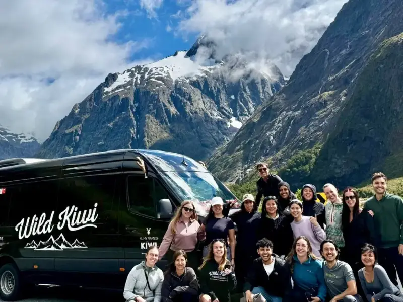 Wild Kiwi small group tour beside a travel van in New Zealand’s South Island, with dramatic mountains, cool alpine scenery and travellers enjoying a scenic winter road trip, highlighting New Zealand as a coolcation destination beyond skiing.