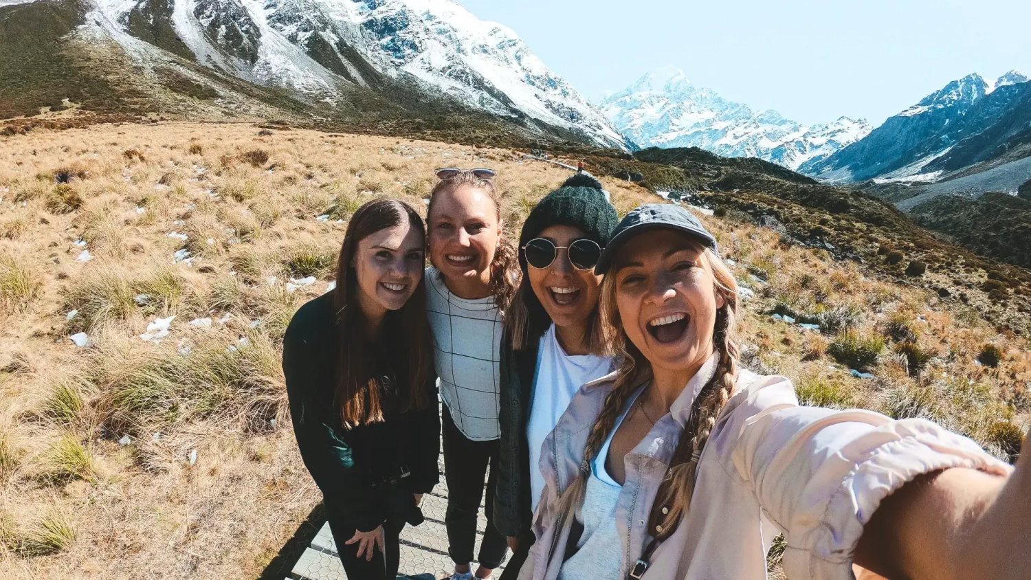 Group of travellers taking a selfie in front of snow-capped mountains on New Zealand’s South Island, highlighting winter travel beyond skiing with alpine scenery, small group adventure, scenic road trip moments and outdoor experiences ideal for a New Zealand winter itinerary.