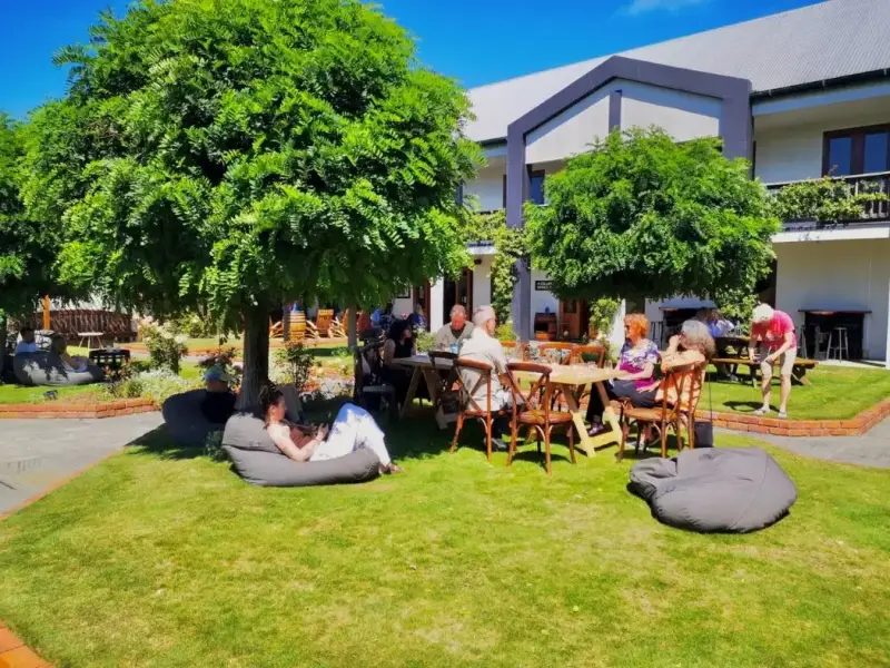 Travellers relax in the sunny garden courtyard at Framingham Winery in Marlborough, New Zealand, sitting at outdoor tables and bean bags beside the cellar door. This image captures the laid-back atmosphere of a Marlborough winery visit, where guests can enjoy New Zealand Sauvignon Blanc, cellar door tastings, and a relaxed food and wine experience in one of the South Island’s best-known wine regions.