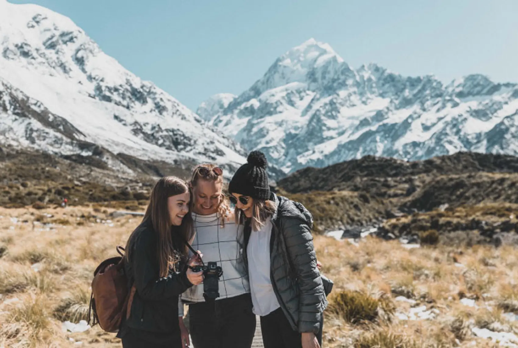 Three friends look at their camera photos in front of mountains in New Zealand