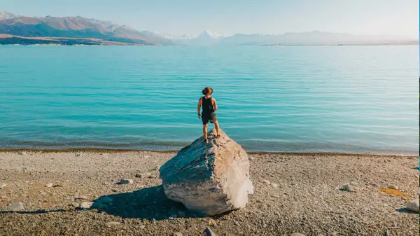 Man standing on a large rock looking out at Lake Tekapo