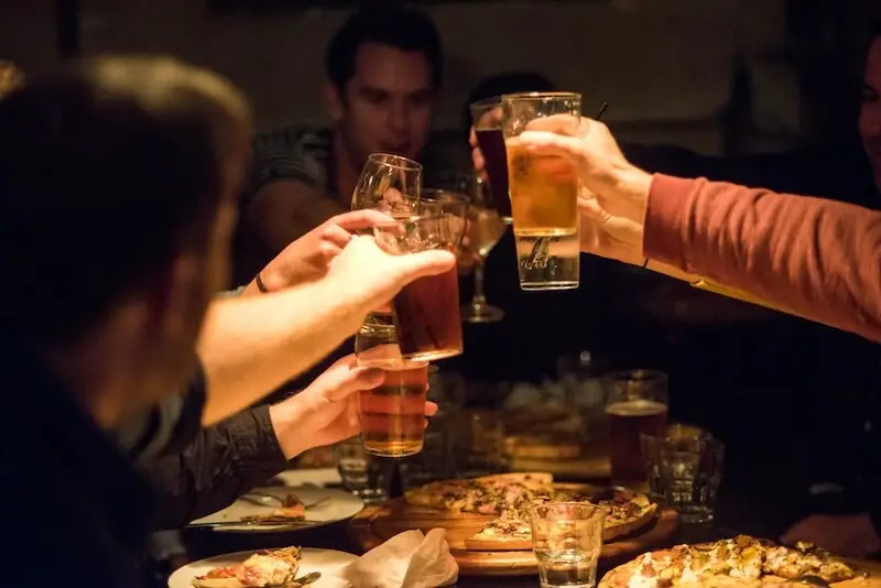 Group of people cheers beers inside of a pub in Queenstown while eating pizza.