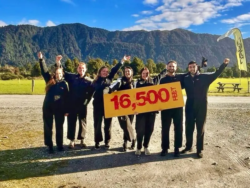 Group of adventure travelles hold a sign after bungy jumping in New Zealand while on a Wild Kiwi tour.